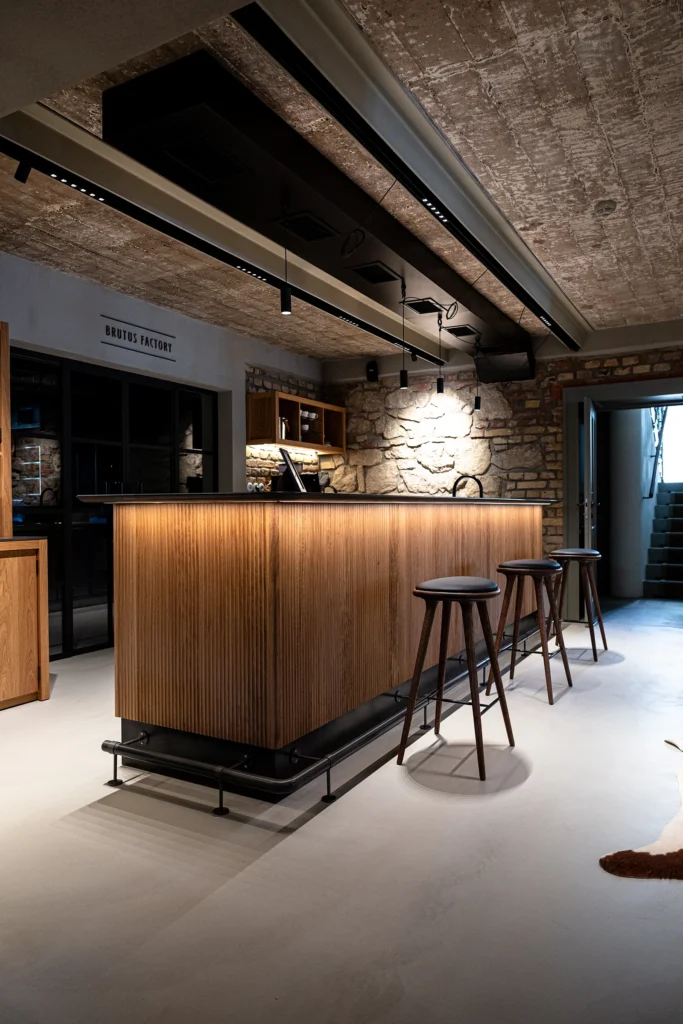 Použitie kameňa okolo barového pultu. Obklad stien z hrubého kameňa a hladká kamenná podlaha v kombinácii s drevom obkladaným barovým pultom a intímnym osvetlením